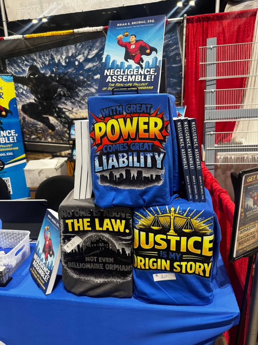 Attorney at Lore t-shirts stacked under a copy of Negligence, Assemble!
