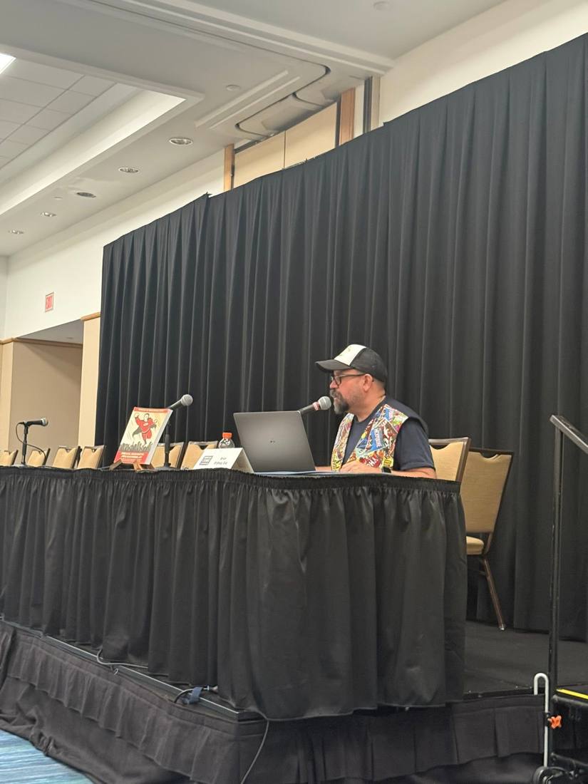Brian at the panel table with a laptop and microphone
